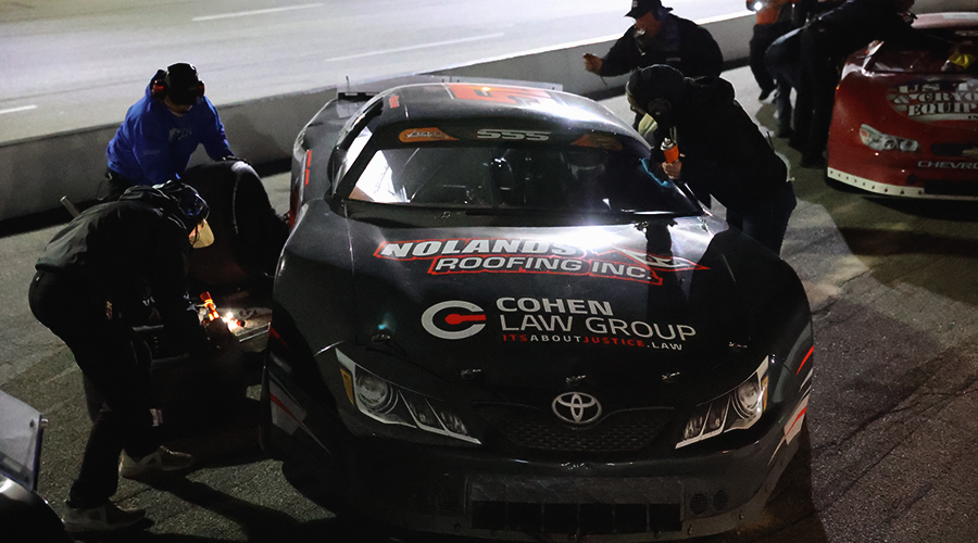 "Jett Noland #50 pit stop at night race with team servicing the car, featuring Noland’s Roofing and Cohen Law Group sponsorships on the hood.