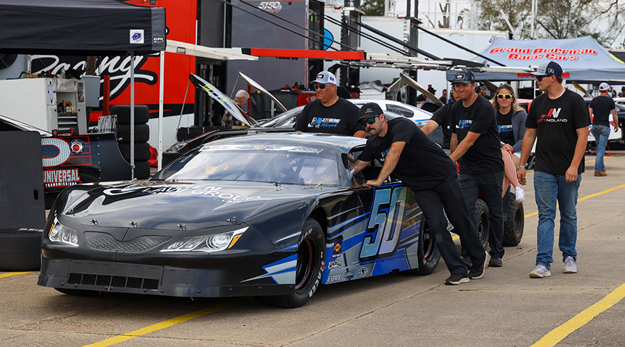 Jett Noland #50 race car being pushed by crew in the pit area before the race, showcasing team preparation and custom black and blue car design.