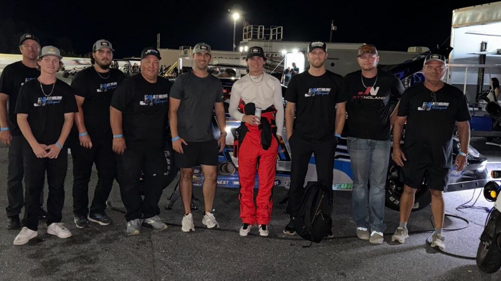 Dawson Spivey makes his debut with Jett Noland Motorsports Driver Development Program, standing with the team in front of the race car under bright lights at the track.